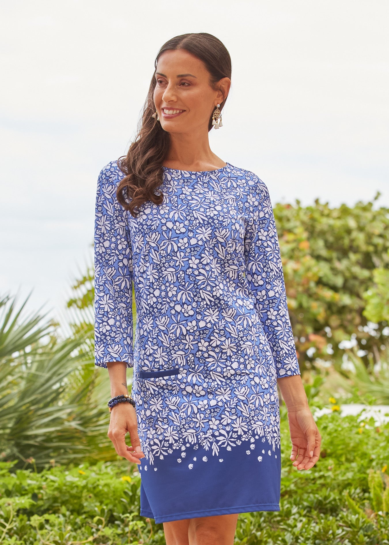 Woman wearing a blue floral dress standing outdoors with greenery in the background