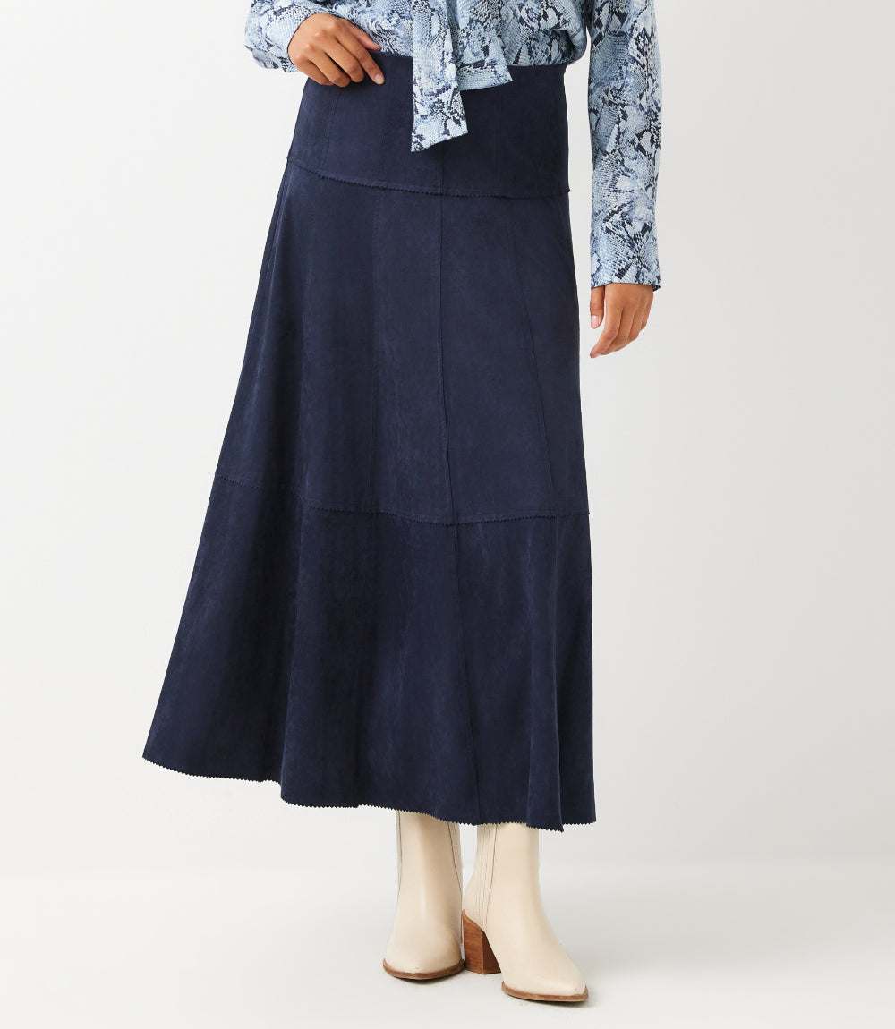 A navy blue midi skirt with a tiered design, styled with a blue patterned blouse and cream ankle boots against a light gray studio background.