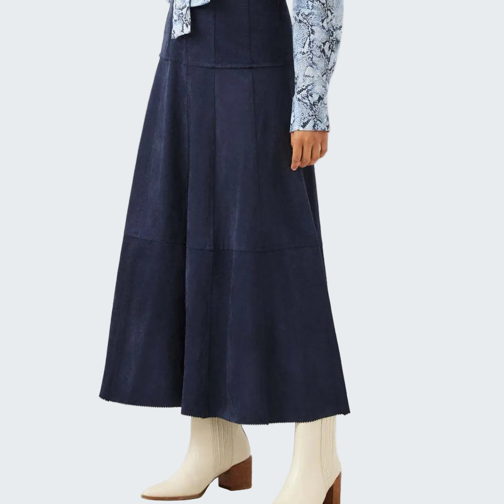 A navy blue tiered A-line skirt worn by a model, styled with a light blue snakeskin print long-sleeve shirt and off-white ankle boots with brown heels, against a plain off-white studio background.