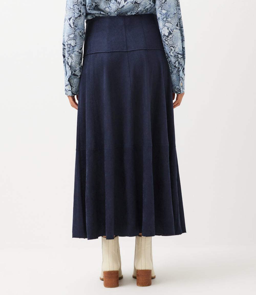 A person shown from the back wearing a dark navy midi skirt, a blue floral long-sleeve top, cream ribbed socks, and brown shoes, against a plain light background.