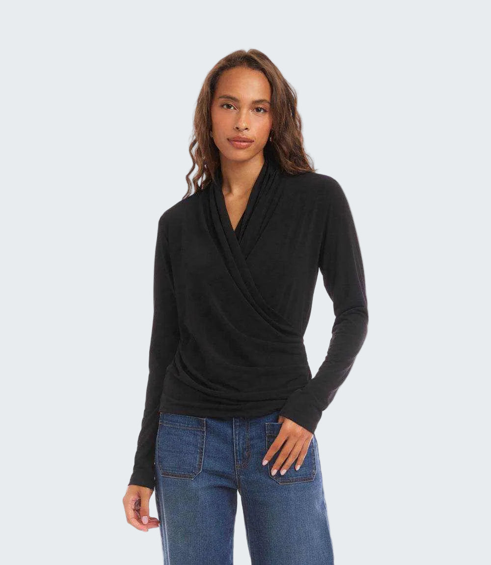 A woman modeling a black long-sleeve wrap-style cowl neck top paired with blue jeans, photographed against a solid white background.