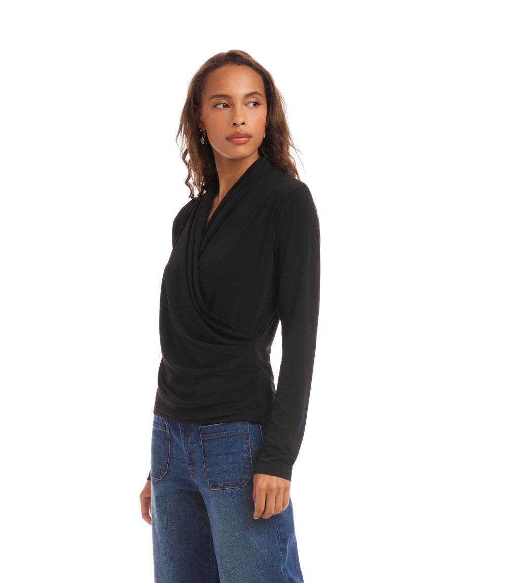 A woman modeling a black long-sleeve wrap-style top with blue jeans against a plain white background.