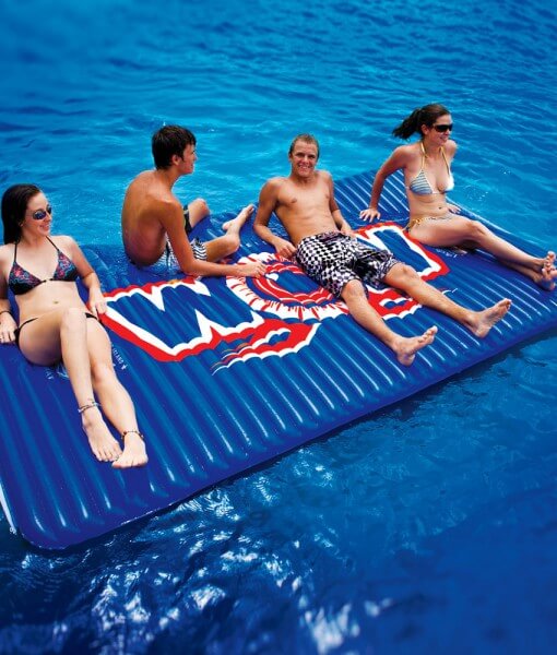 Four people relaxing on a large inflatable pool mat with a logo in the water.