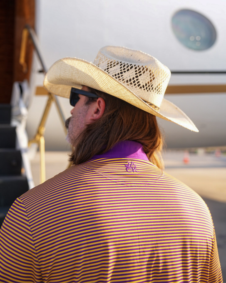 Man wearing a straw cowboy hat and striped shirt in front of an airplane