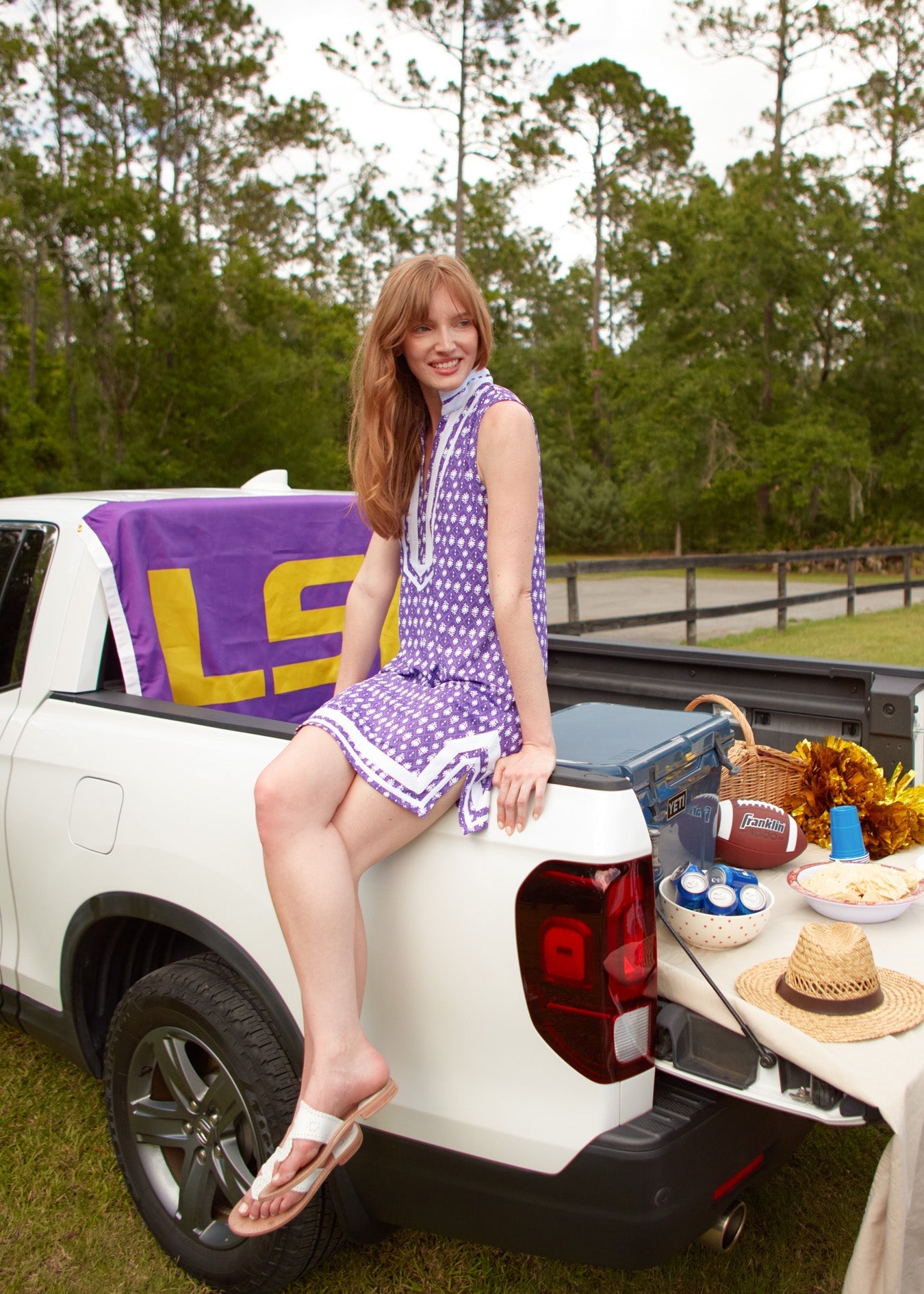 Woman sitting in the bed of a white pickup truck with sports gear and a LSU towel.