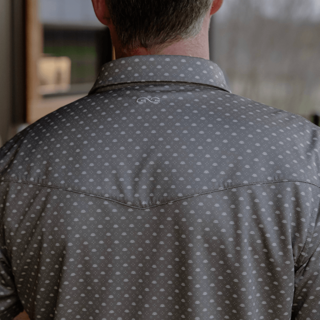 Person wearing a gray patterned shirt with a brand logo, facing away from the camera.