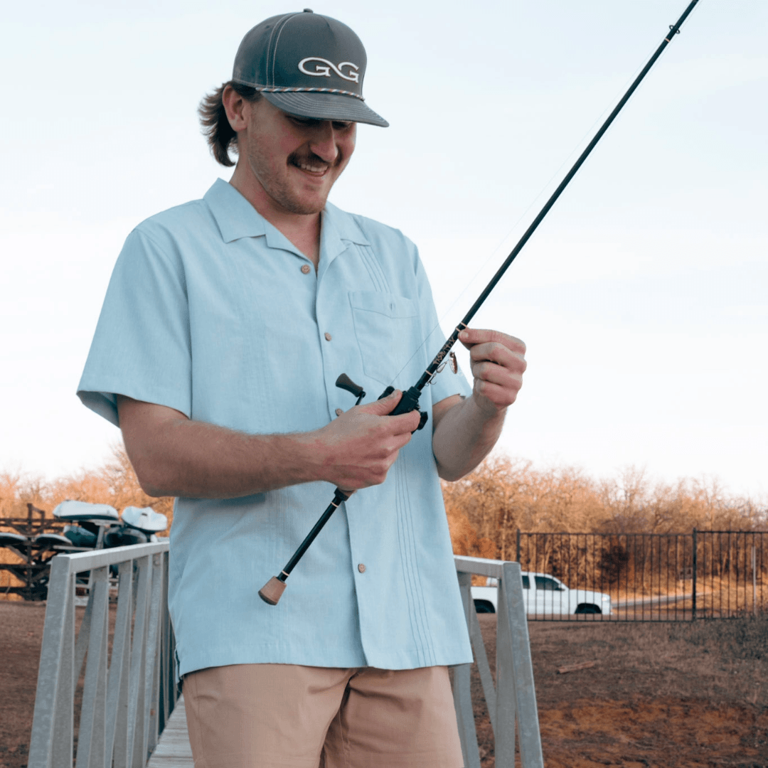 Man holding a fishing rod on a wooden deck with a scenic background