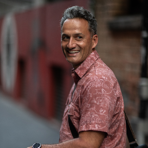 Man in a patterned shirt smiling outdoors with a blurred background