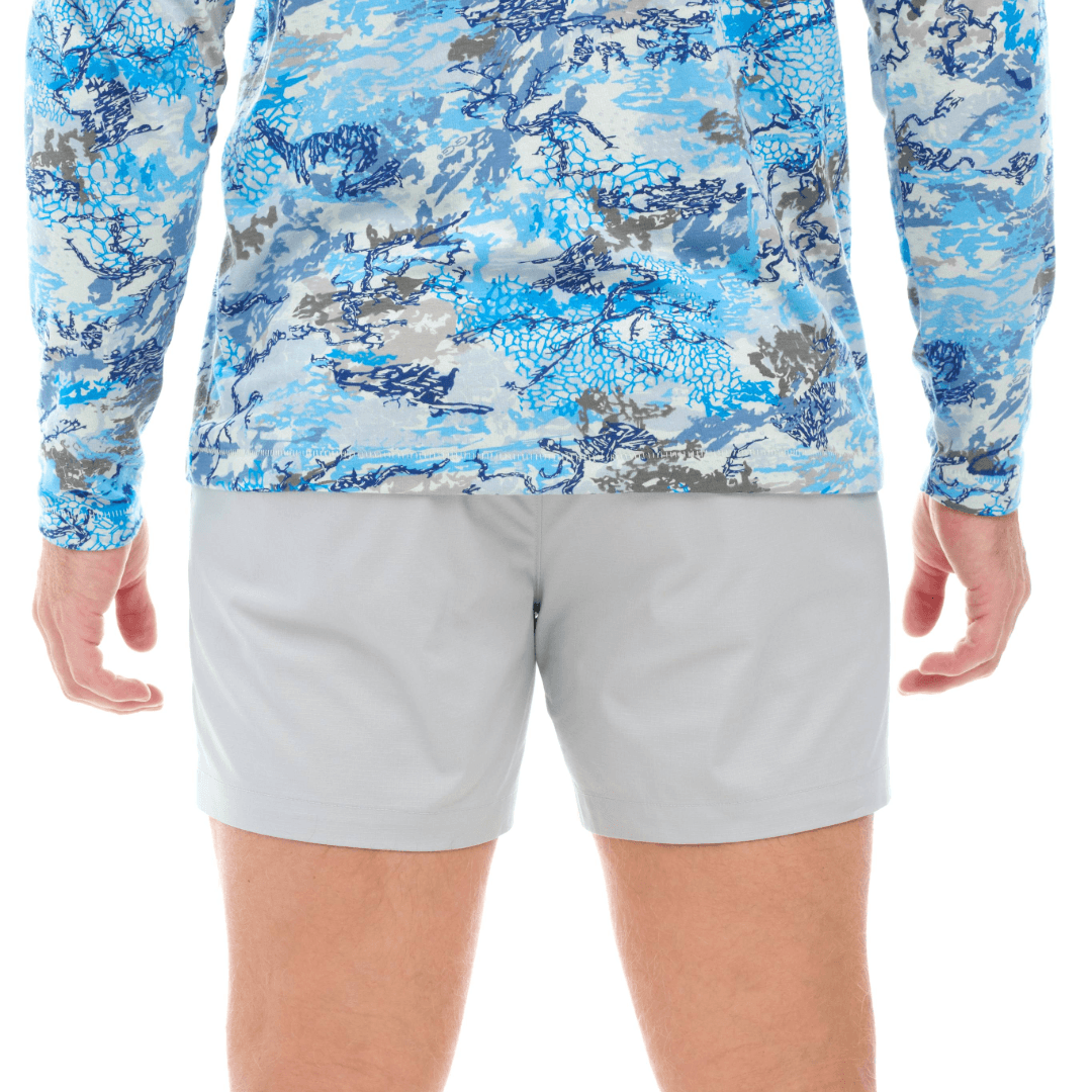 Person wearing a blue camouflage long-sleeve shirt and gray shorts on a white background