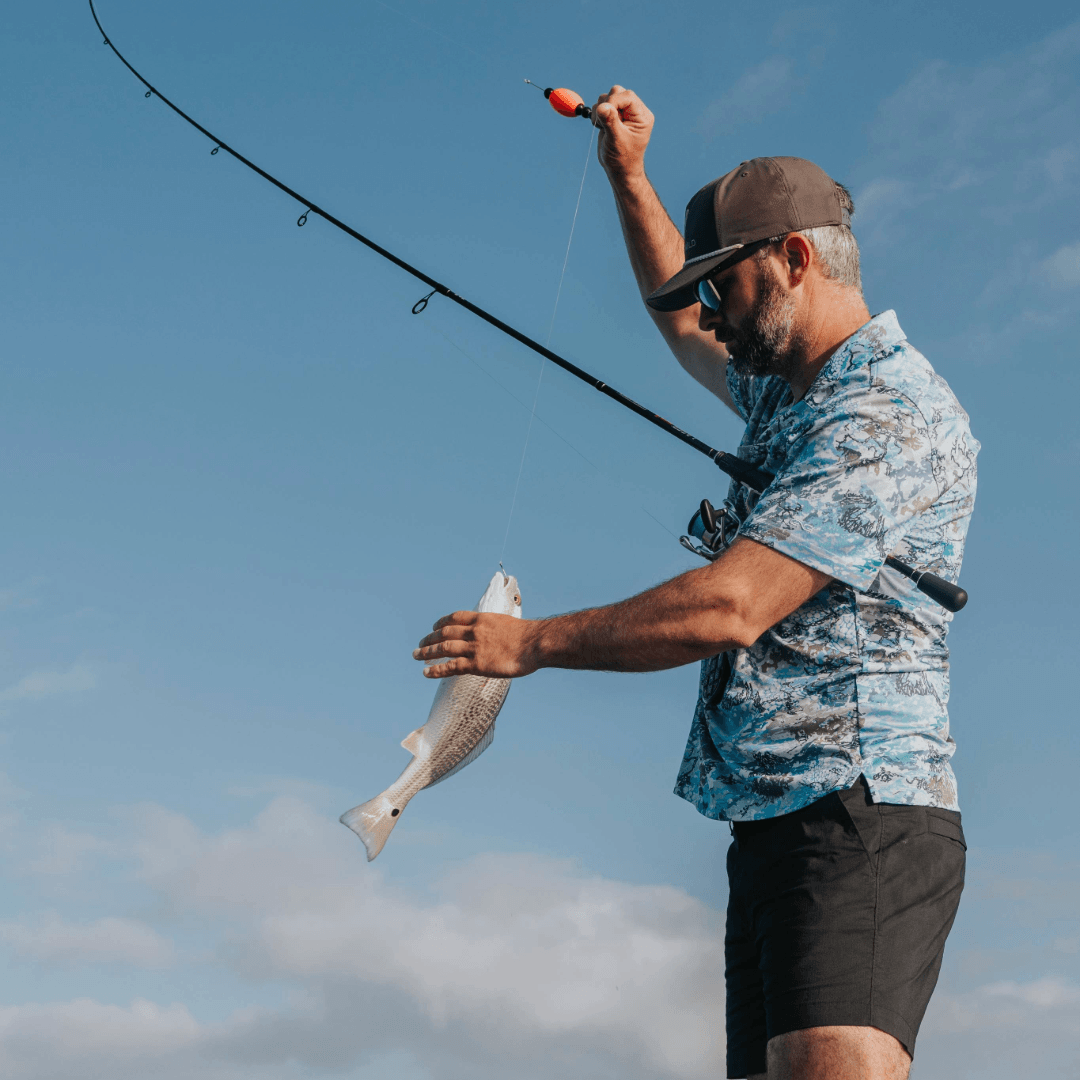 Man holding a fish and fishing rod against a blue sky