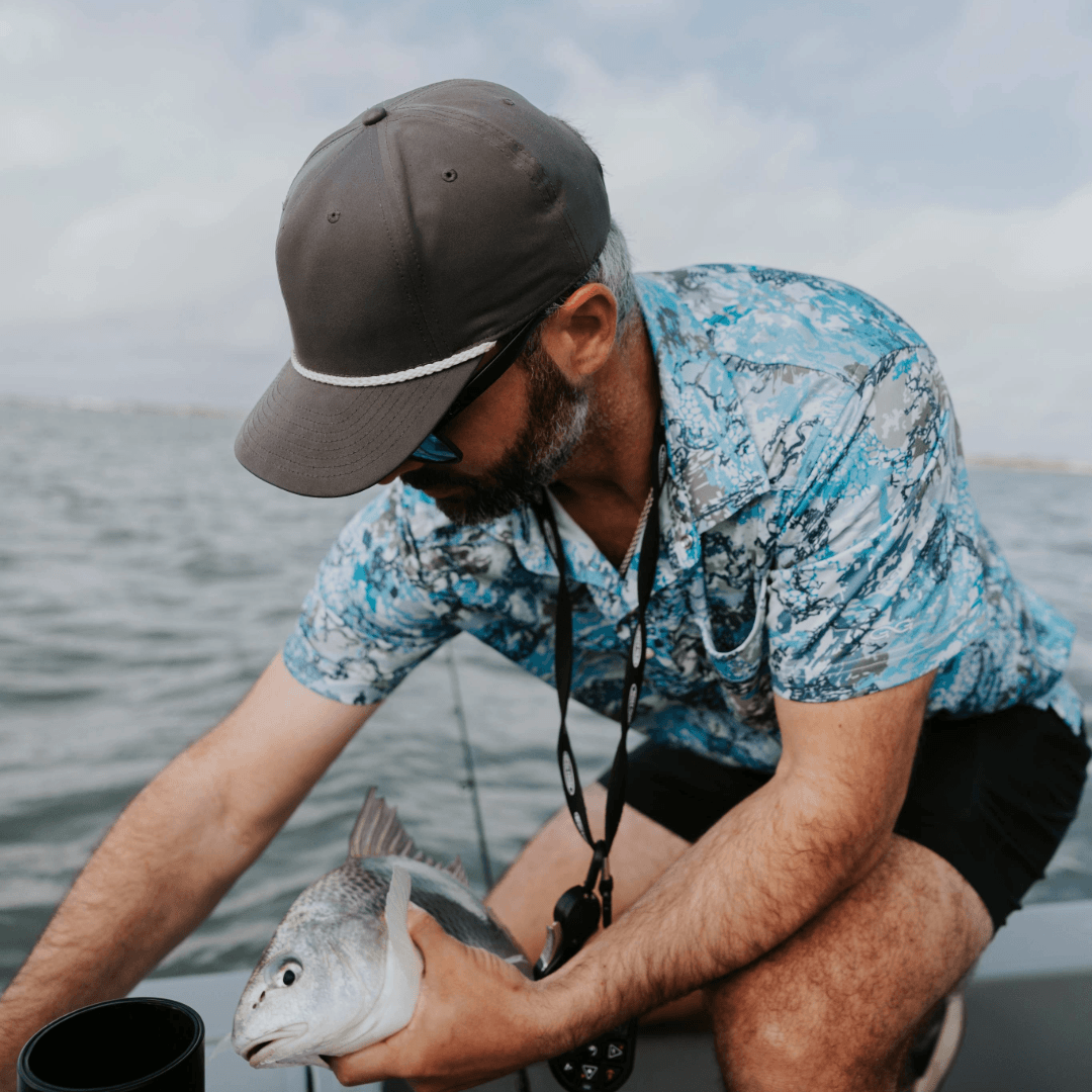 Man on a boat holding a fish with water and sky in the background