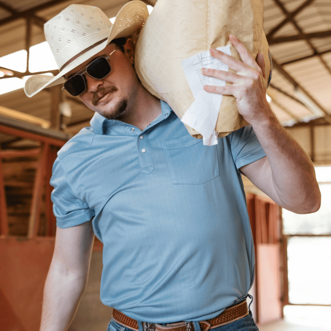 Man wearing a cowboy hat and sunglasses, holding a large beige hat against his chest.