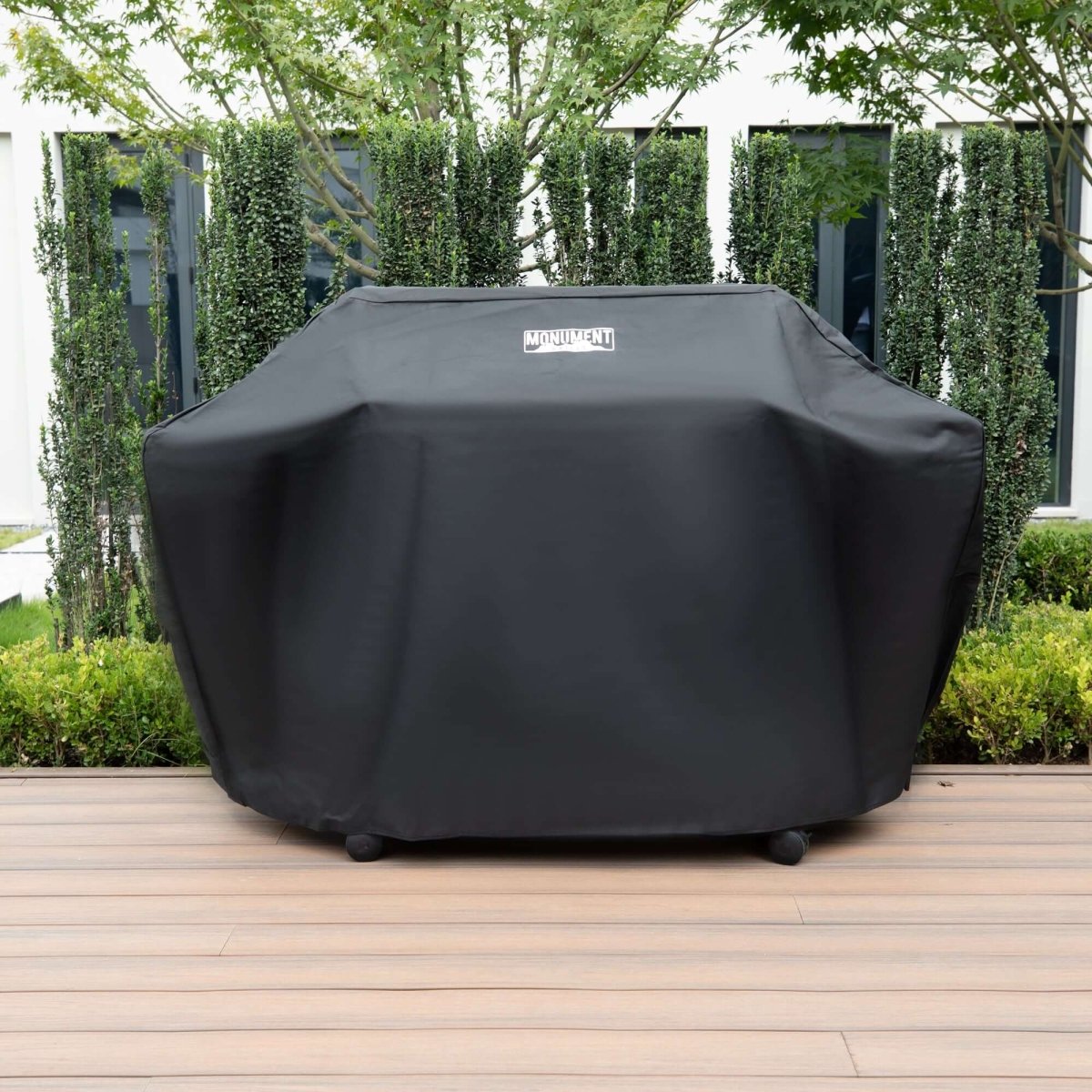 Black grill cover on a wooden deck with greenery in the background