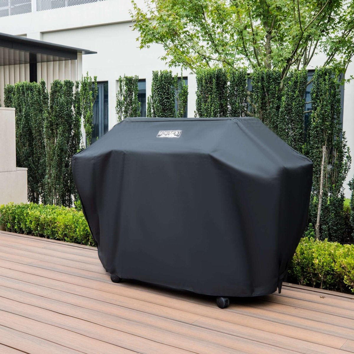 Black grill cover on a wooden deck with greenery in the background