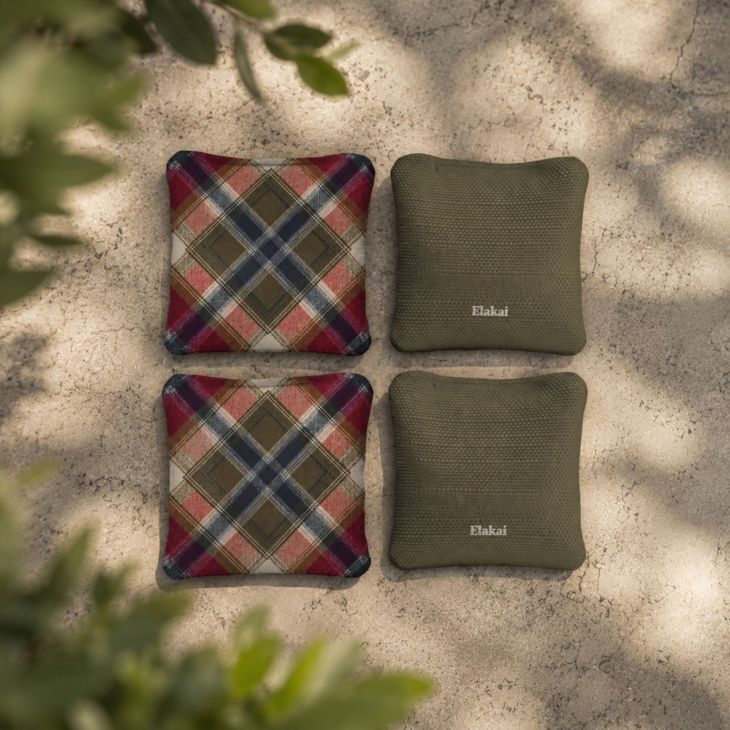 Two plaid patterned pillows and two green textured pillows on a stone surface with plant shadows.