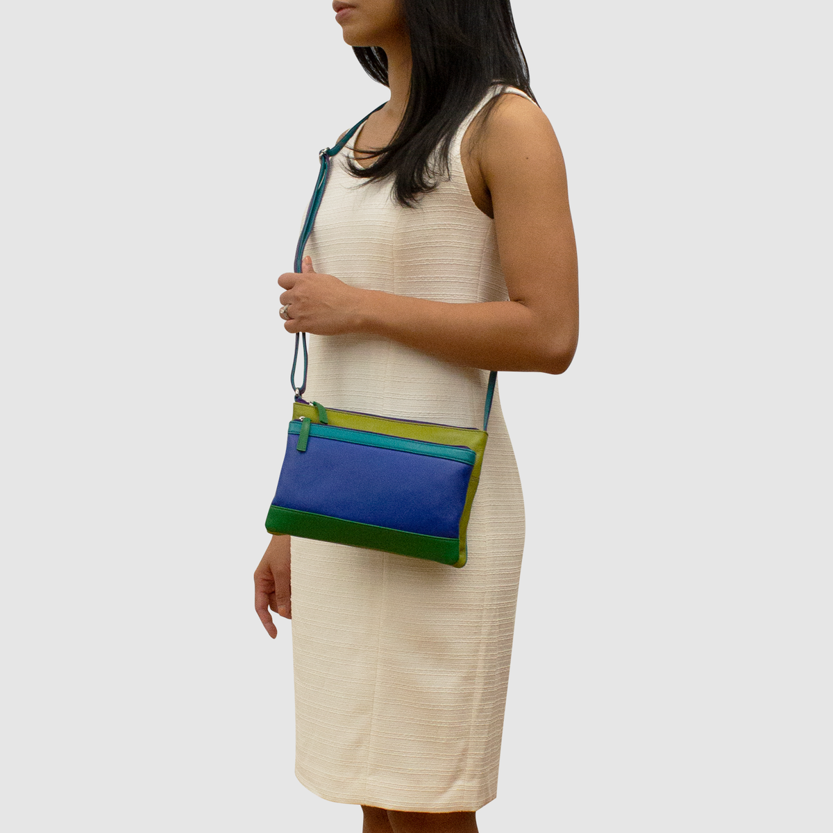Woman holding a blue and green handbag against a plain background