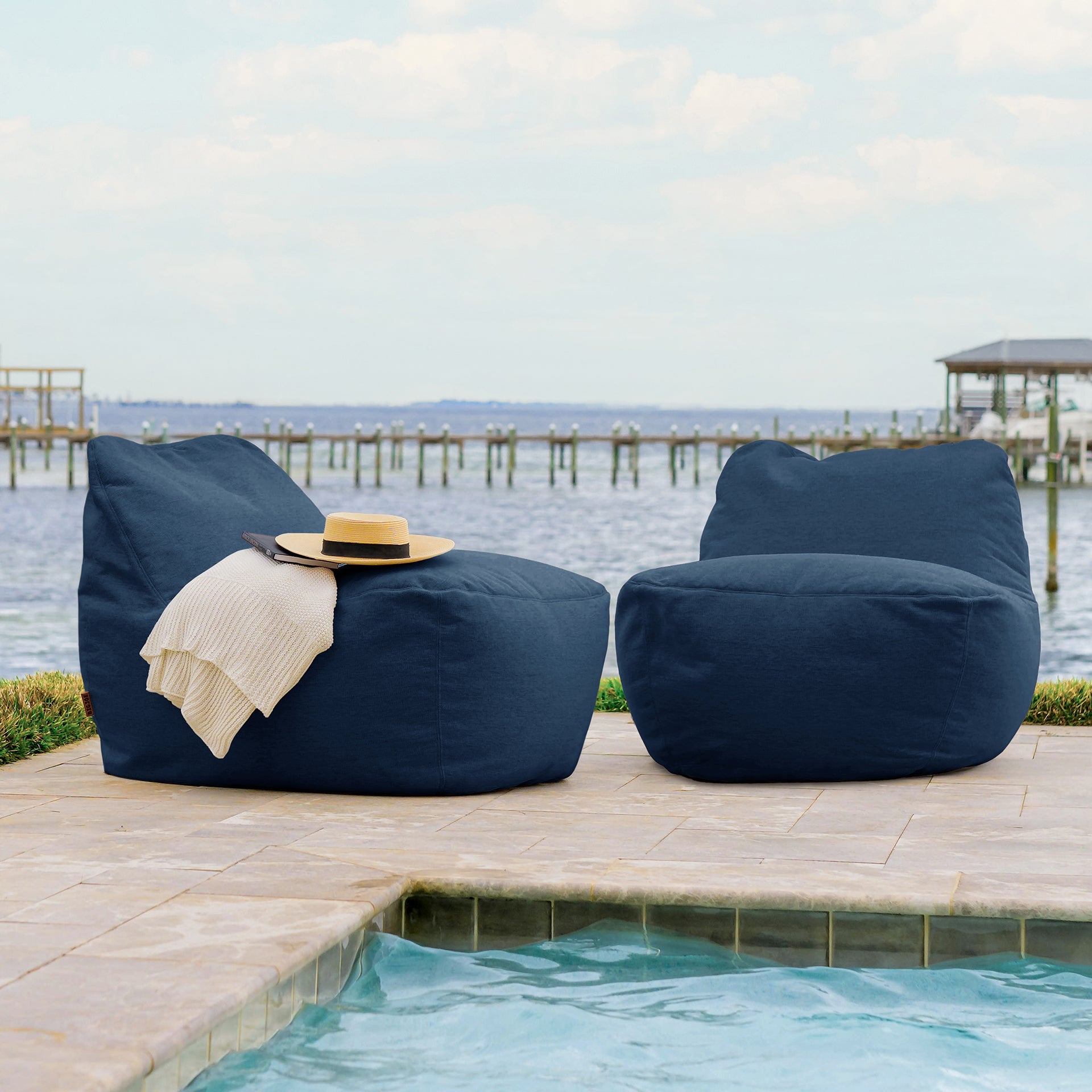 Two navy bean bags on a patio by a pool with a scenic background