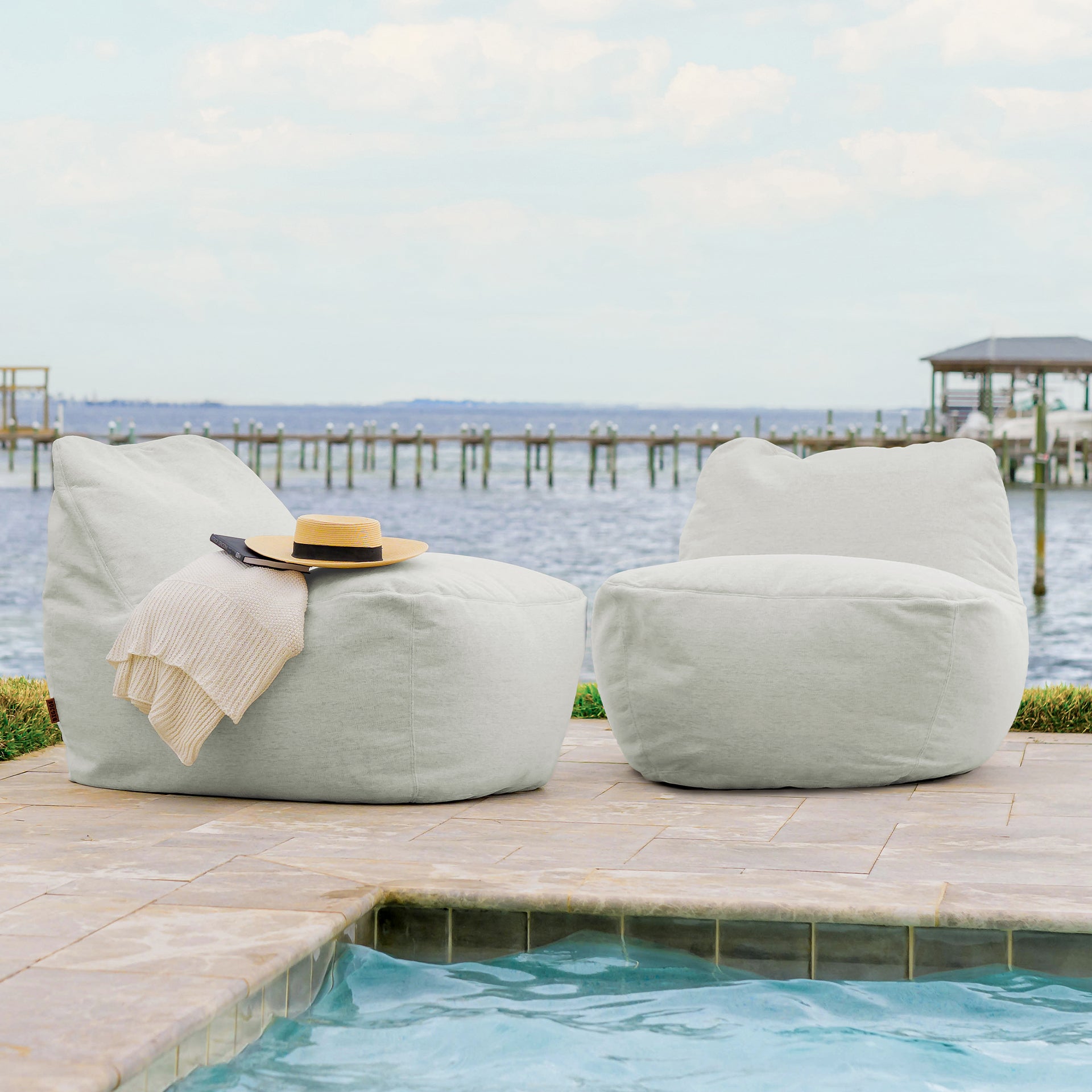 Two light gray bean bags on a patio by a pool with a scenic background.
