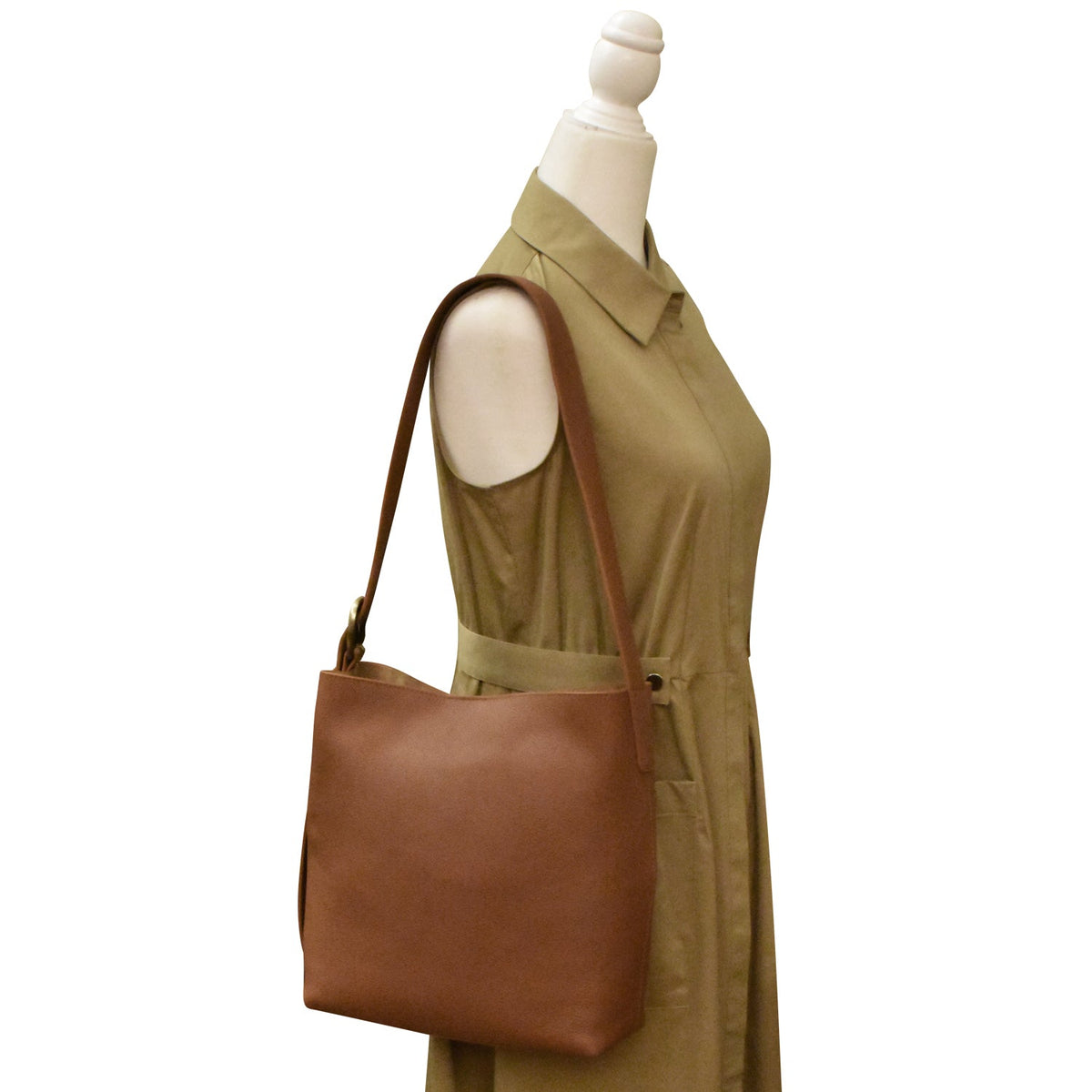 Brown leather handbag on a mannequin with a beige dress against a white background