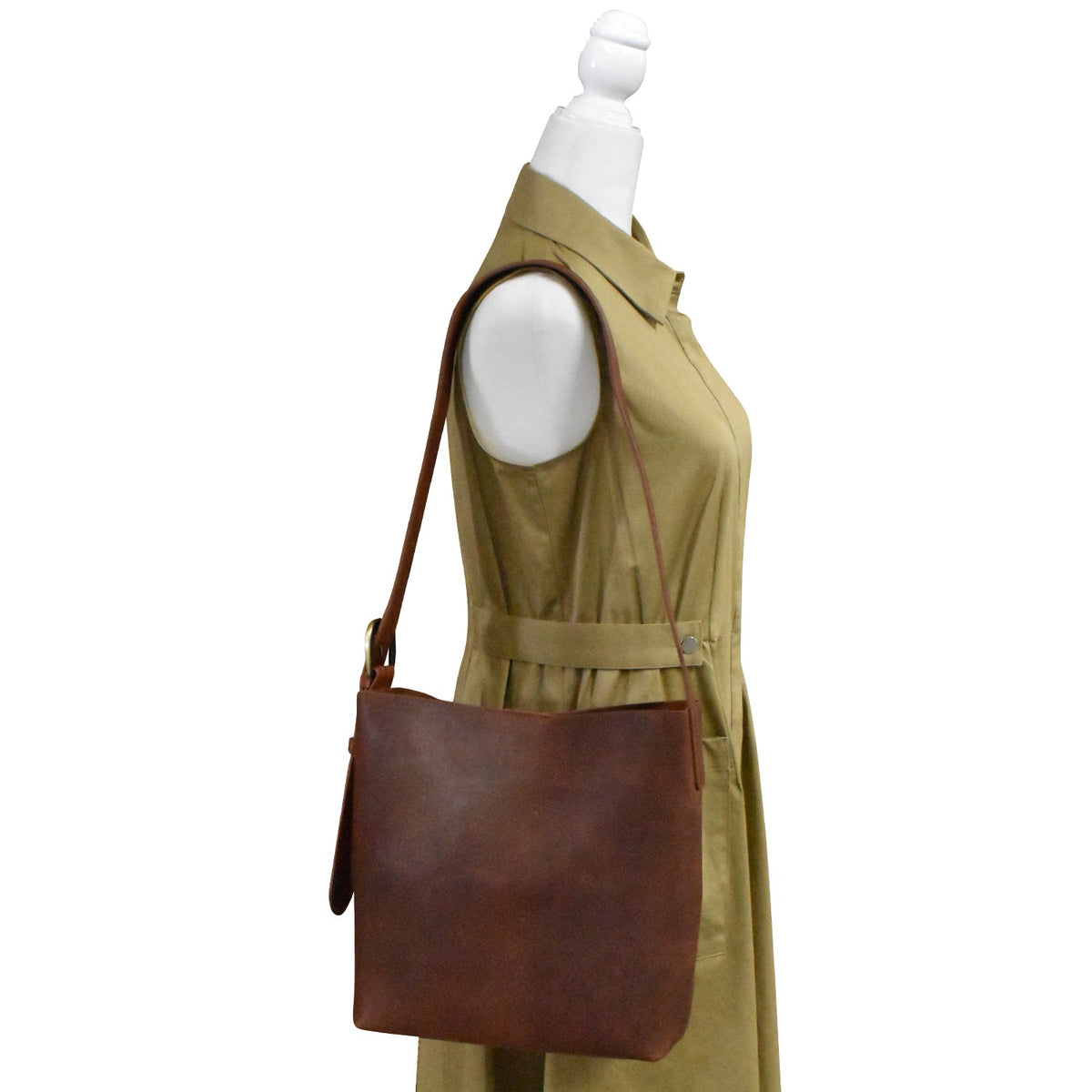 Brown leather handbag on a mannequin wearing a beige dress against a white background