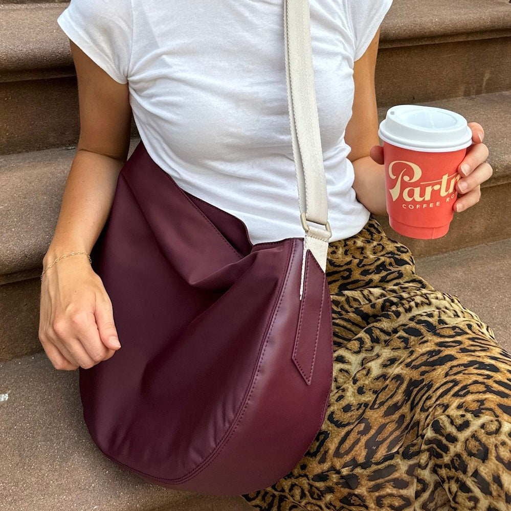 Person holding a red coffee cup with 'Party' branding, sitting on steps with a maroon handbag.