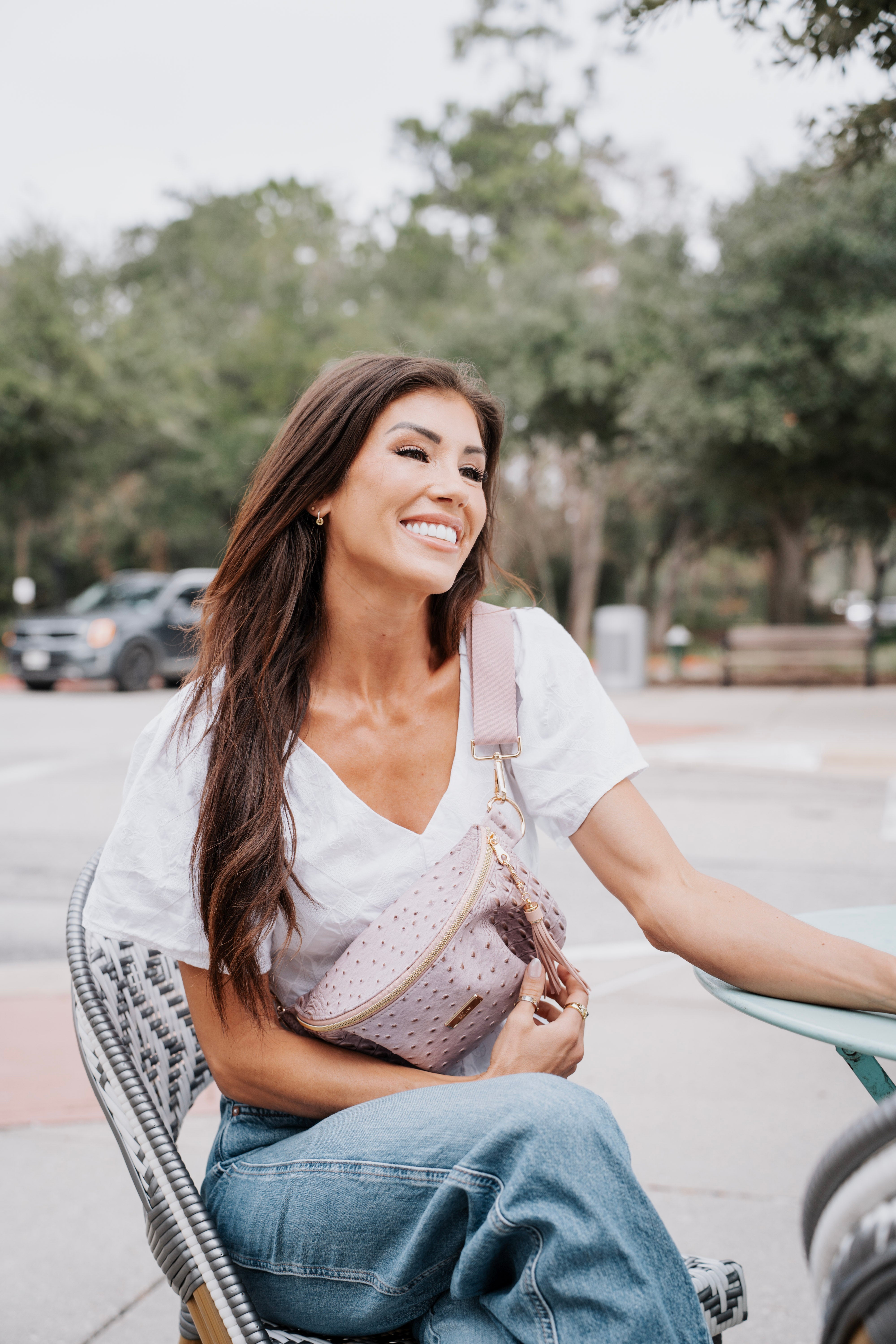 Woman sitting outdoors holding a pink handbag, smiling.