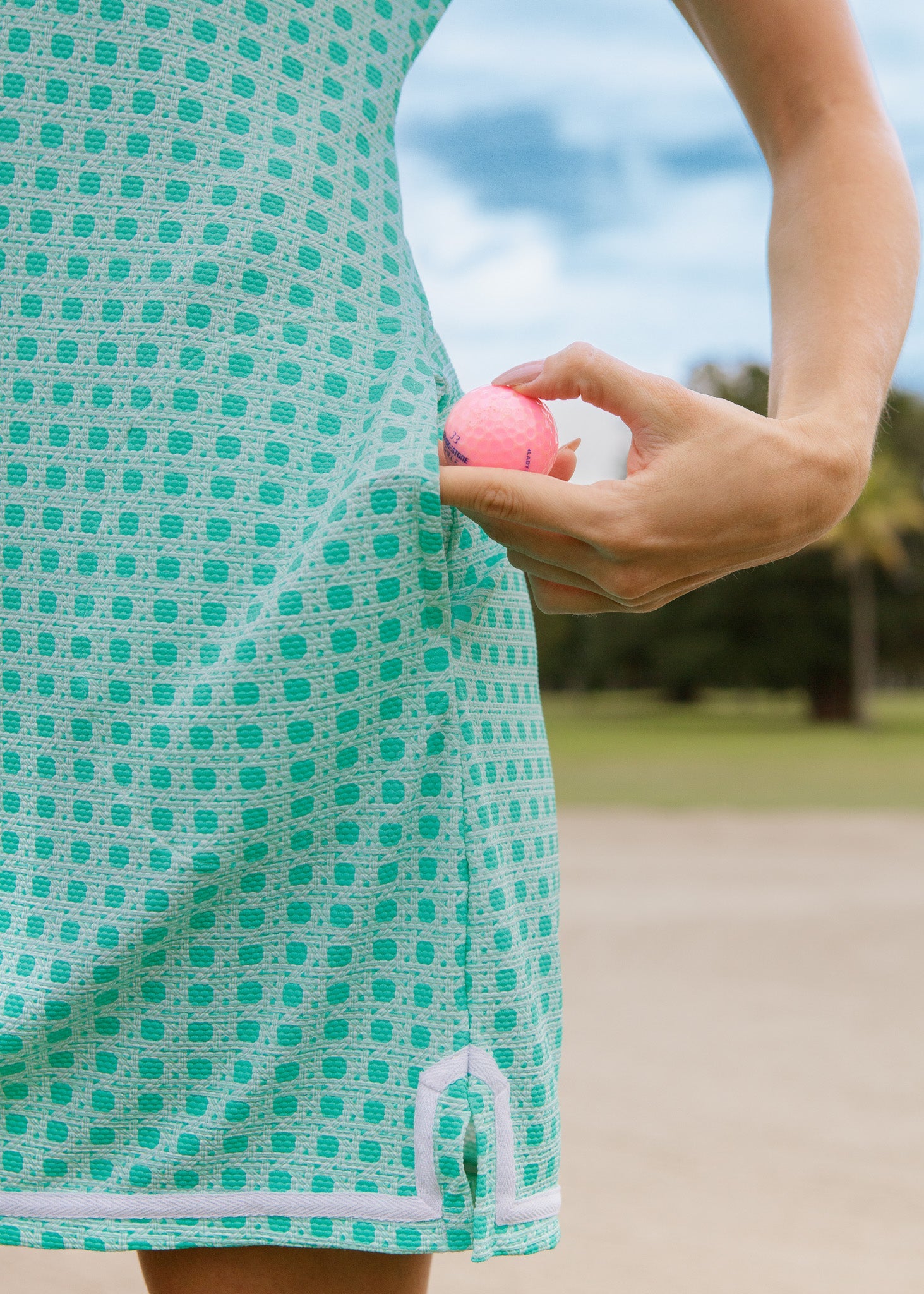 Person holding a pink ball with a green patterned outfit in a park setting