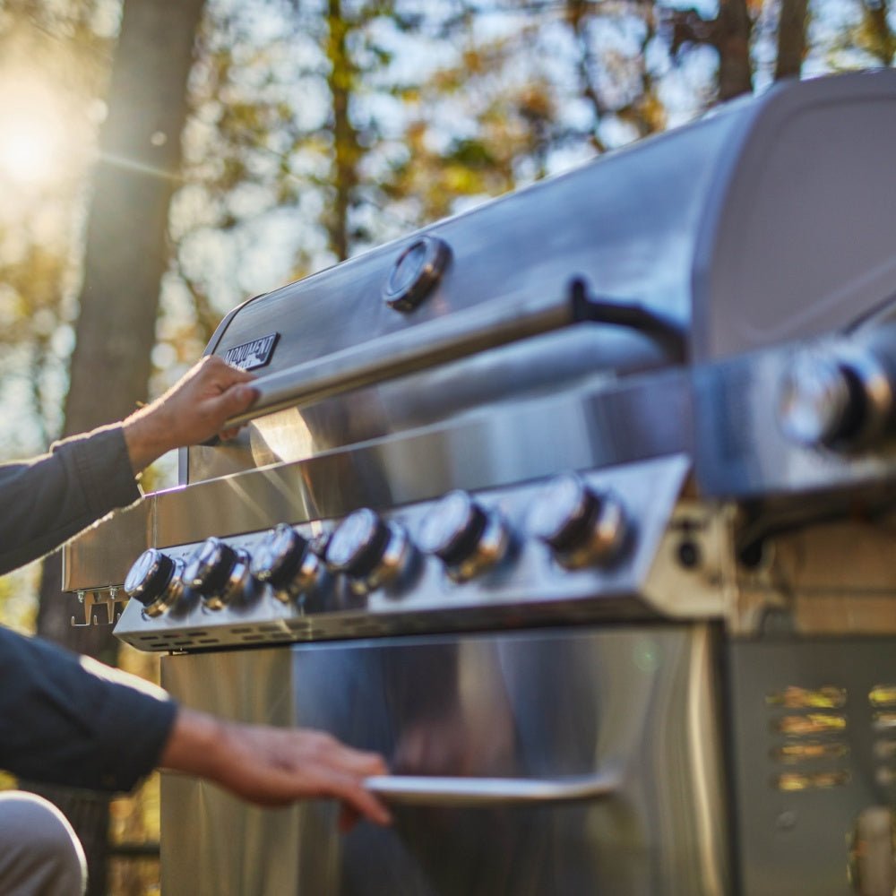 Person opening a large outdoor grill with trees in the background