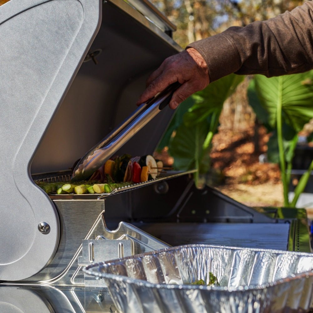 Person grilling vegetables on an outdoor grill with a scenic background