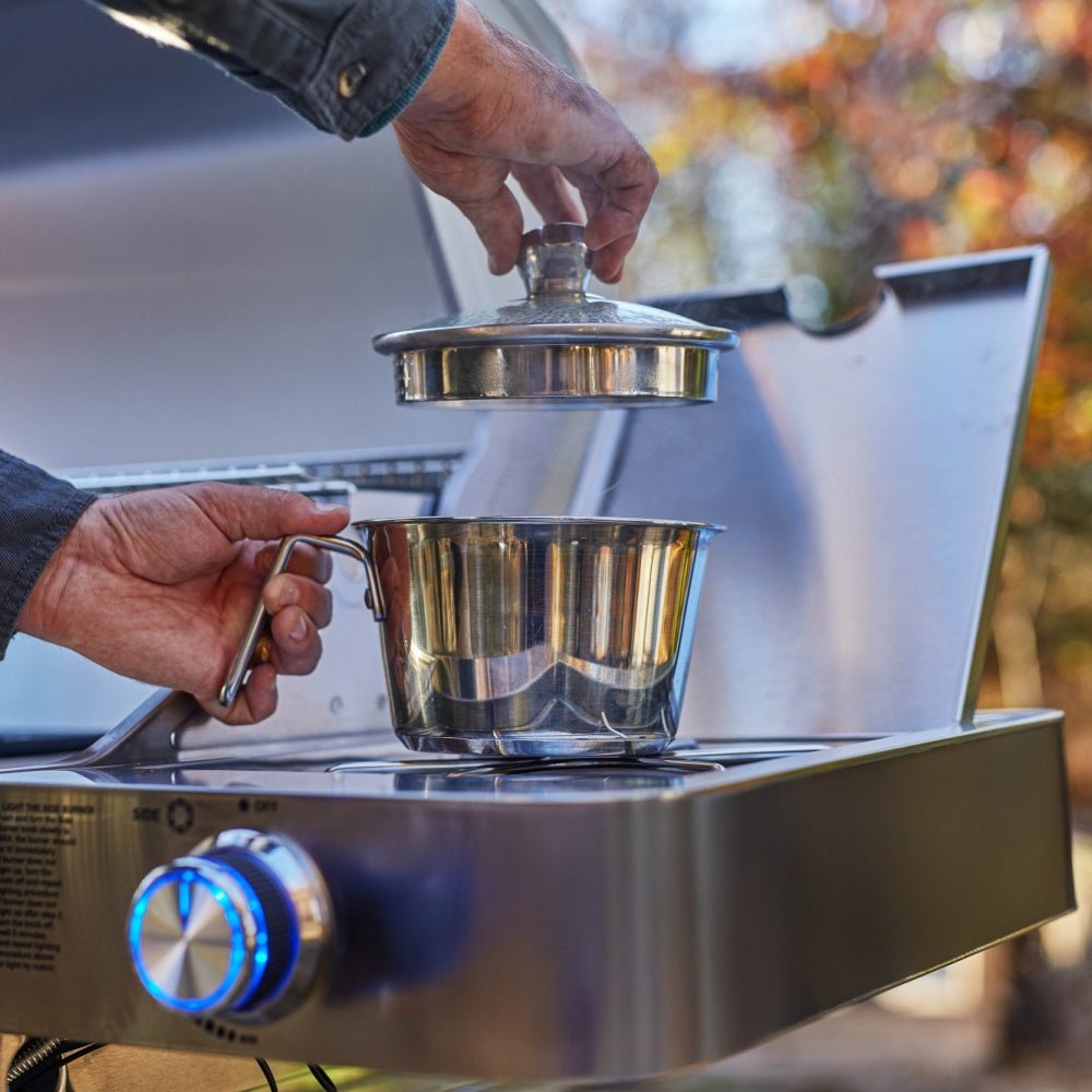 Stainless steel coffee maker on a portable stove with a blurred outdoor background