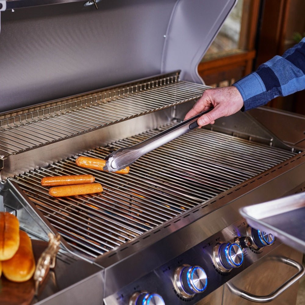 Person grilling hot dogs on a stainless steel barbecue grill.