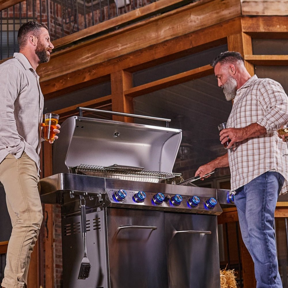 Two men standing next to a large barbecue grill in an indoor setting.