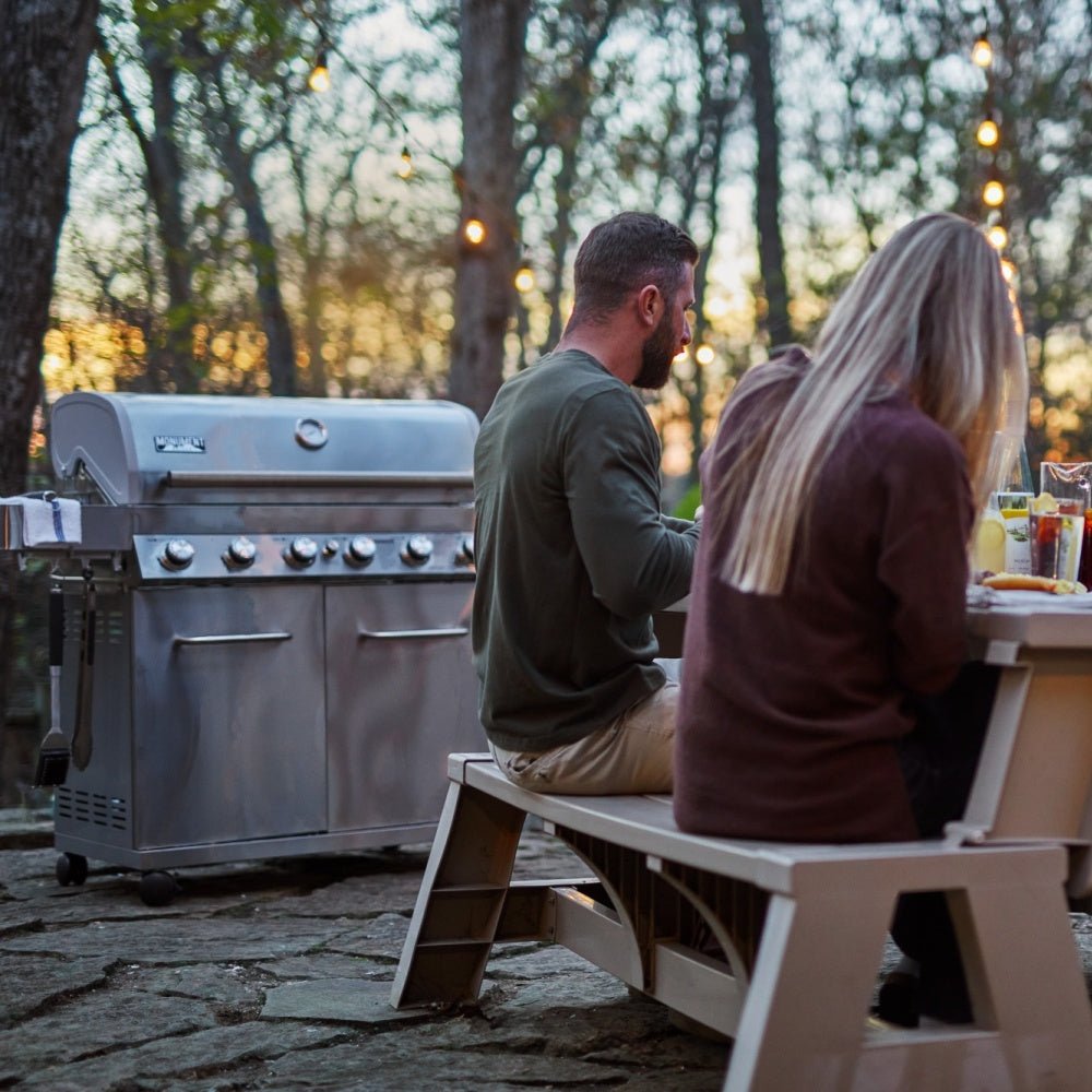 Two people sitting on a bench next to a barbecue grill outdoors.