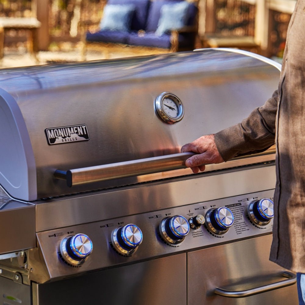 Stainless steel grill with a person opening the lid outdoors