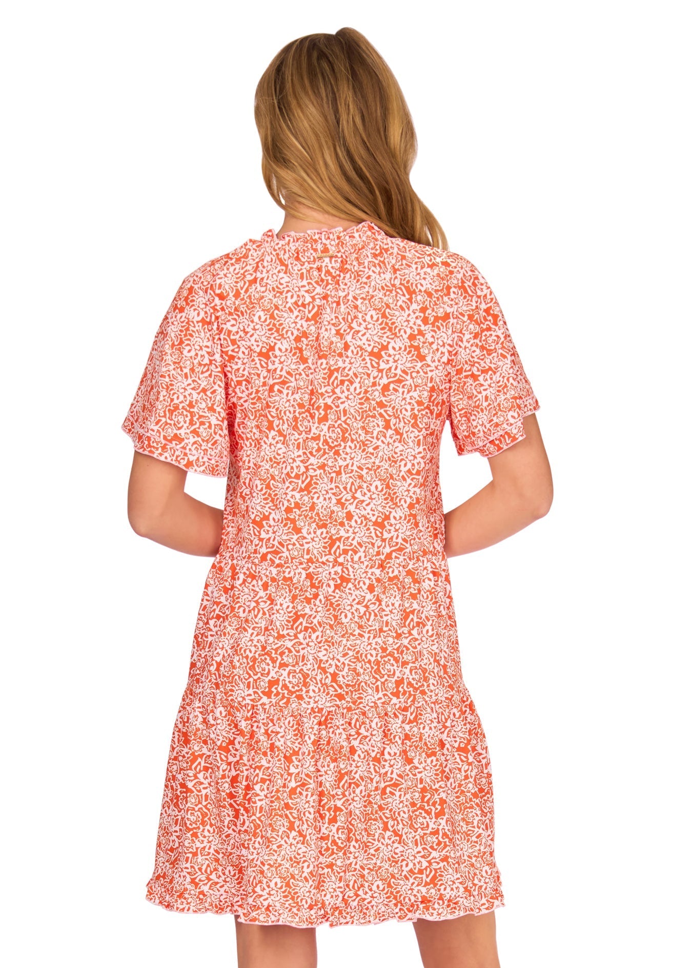 A woman viewed from behind wearing a short-sleeve A-line dress with a dense orange and white floral print, set against a plain white background.