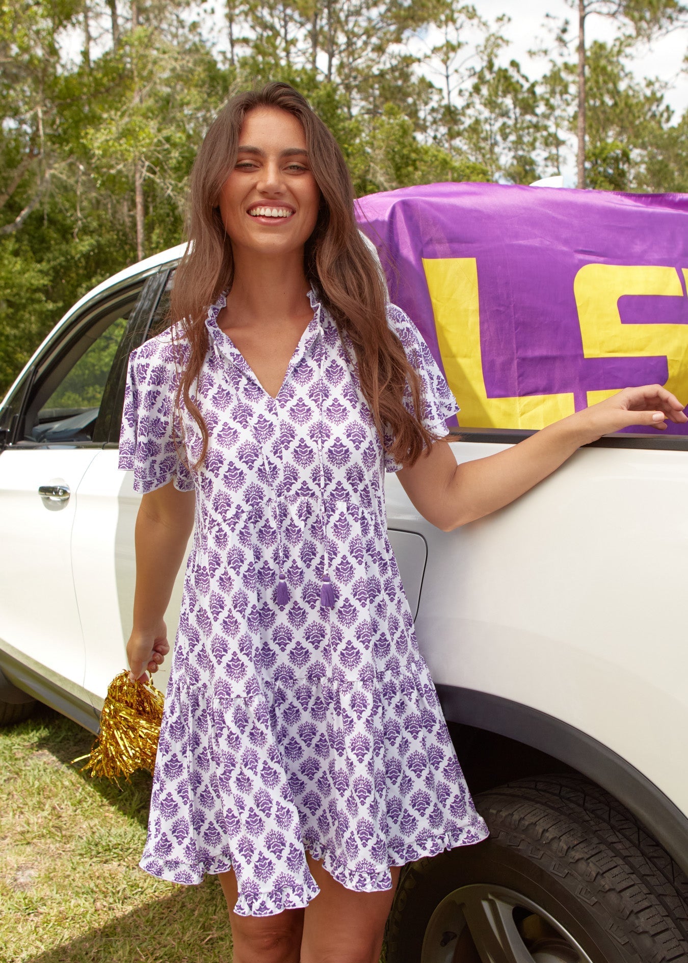 Woman in a purple patterned dress standing next to a car with a LSU towel.