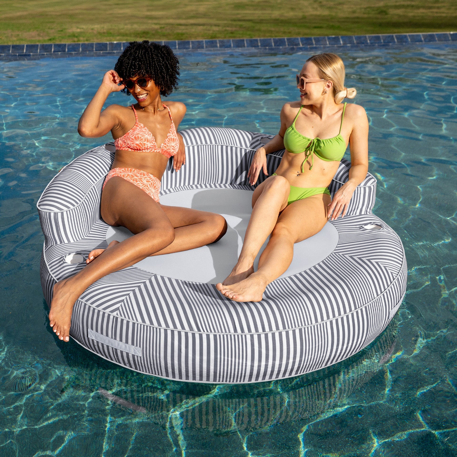 Two women sitting on a striped pool float in a pool