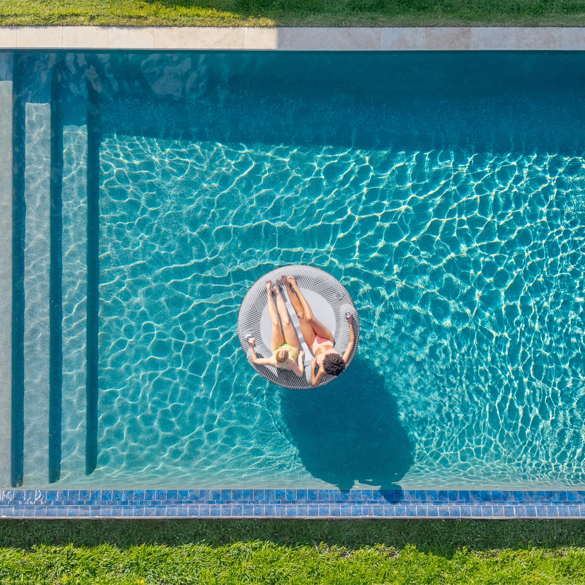Person floating on a pool float in a clear blue pool with green grass surrounding it