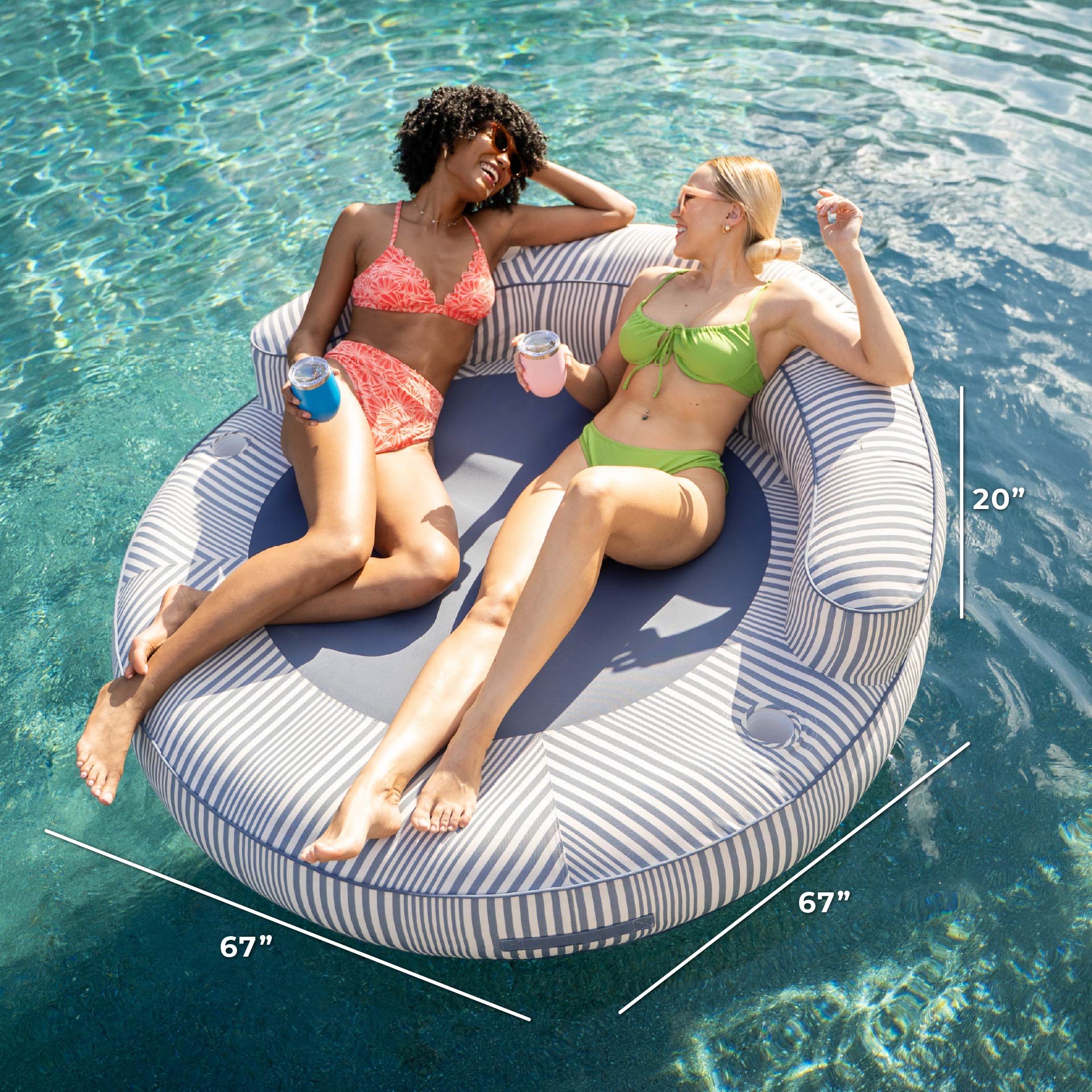 Two women lounging on a circular striped pool float with measurements displayed.