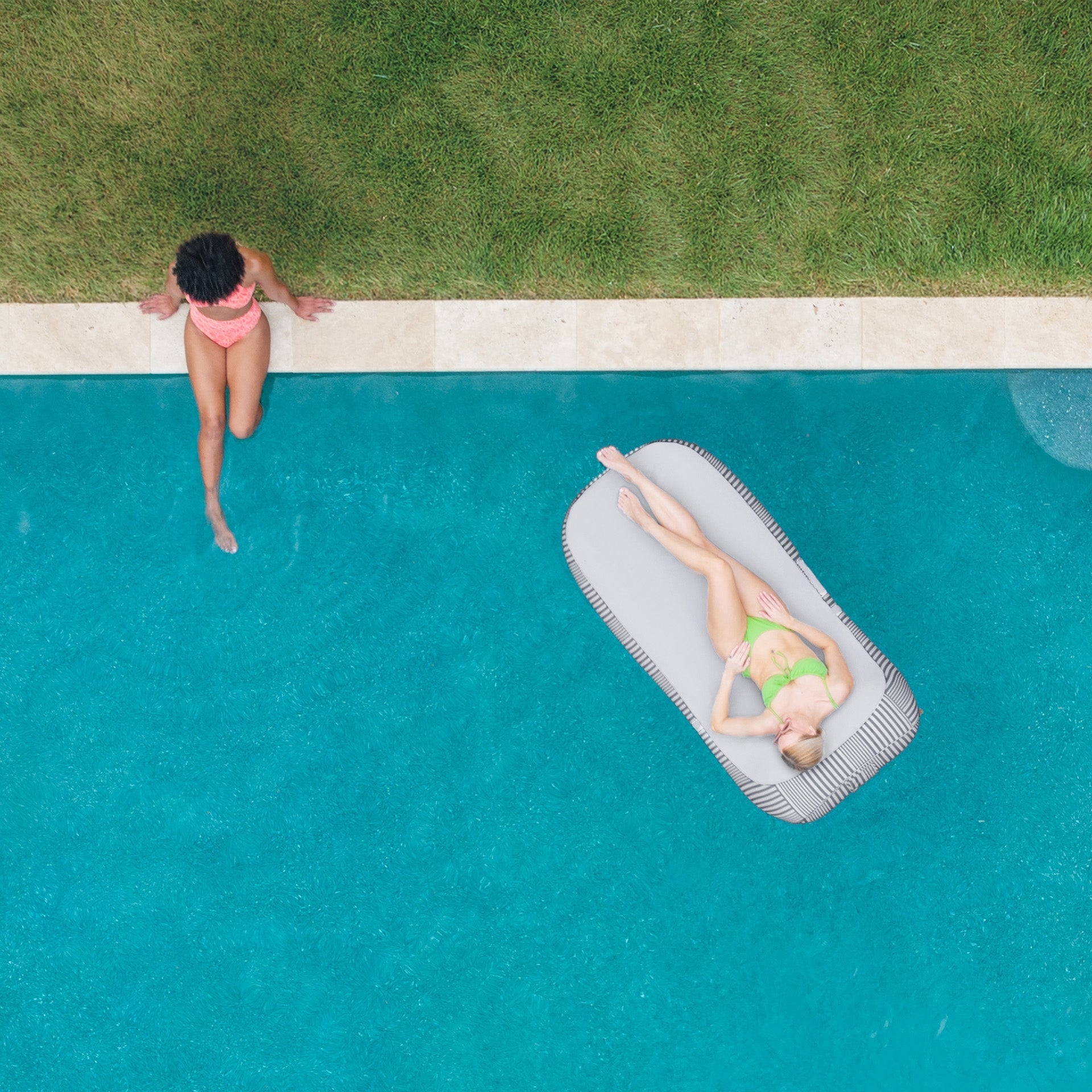 Two people by a pool, one standing and one lying on an inflatable raft.