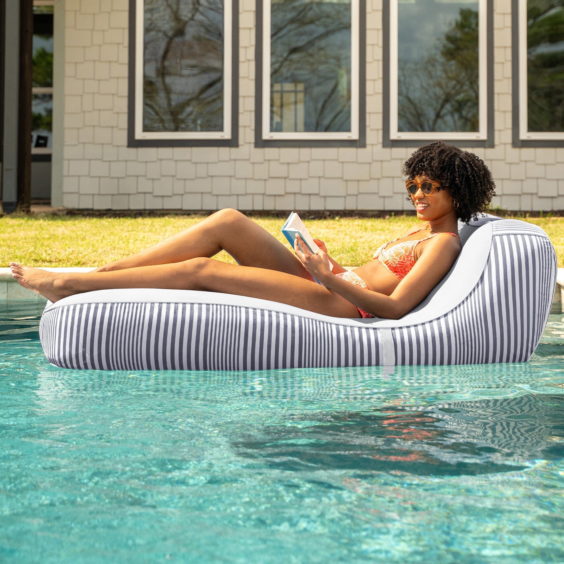 Woman lounging on a striped inflatable pool float in a pool with a house in the background