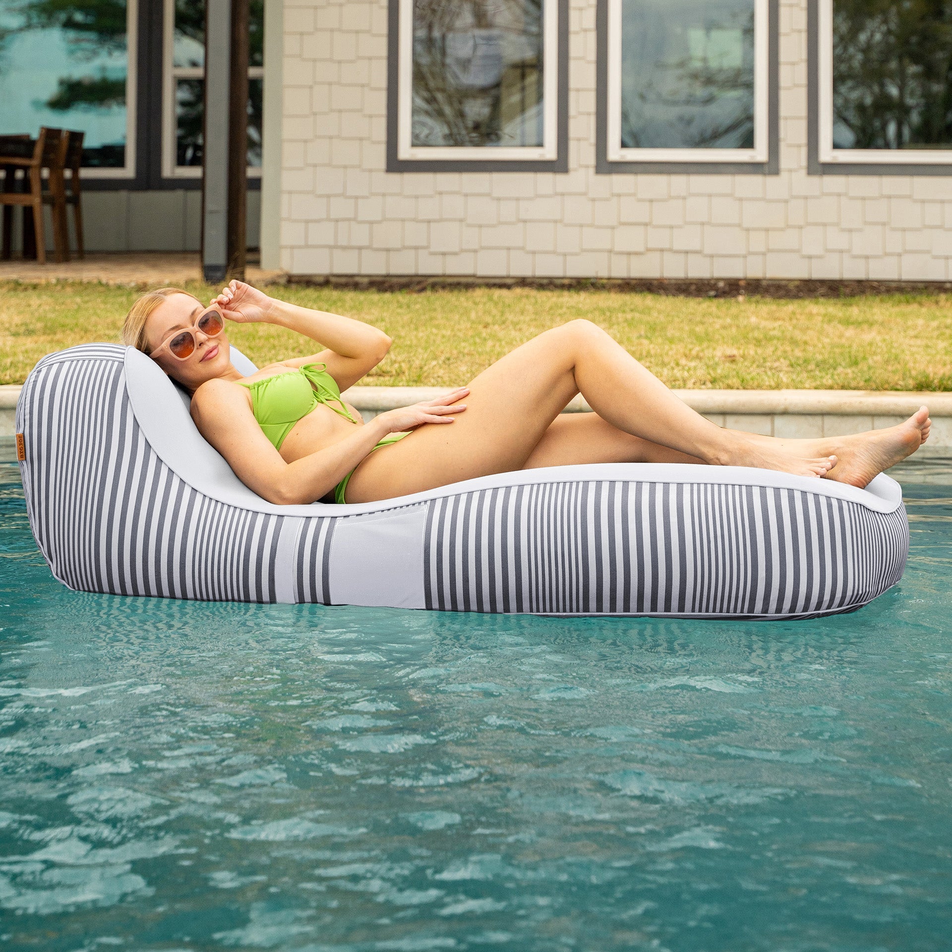 Woman lounging on a striped pool float in a pool with a house in the background