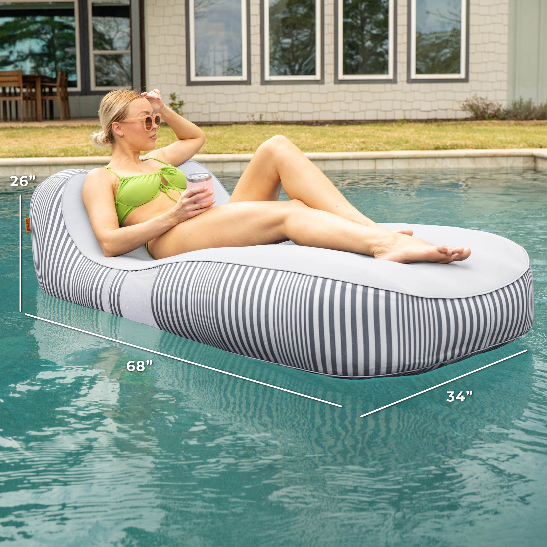 Woman lounging on a striped pool float with dimensions displayed, set against a poolside background.