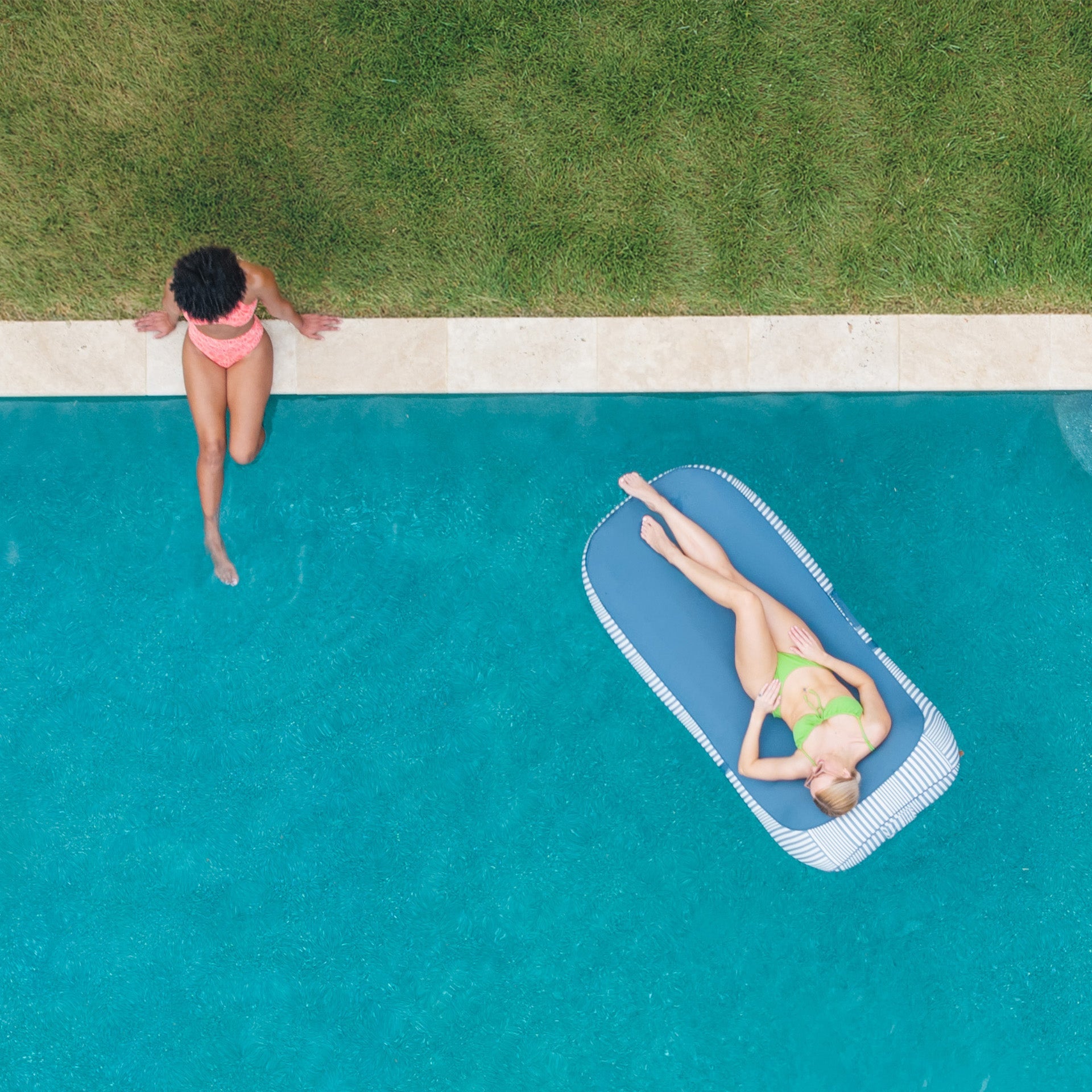 Two people by a pool, one standing and one lying on a floatie.