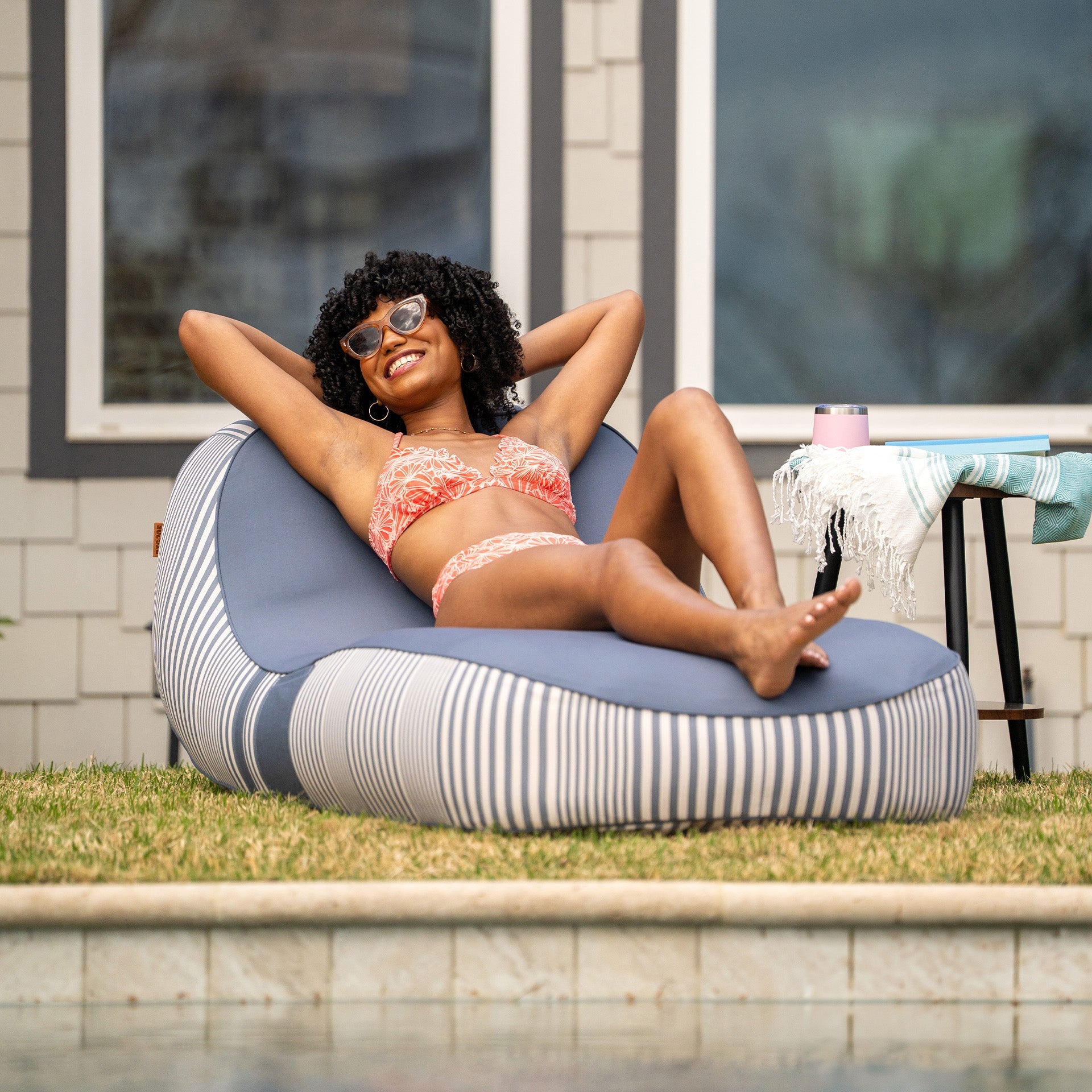Woman relaxing on a striped bean bag by a poolside