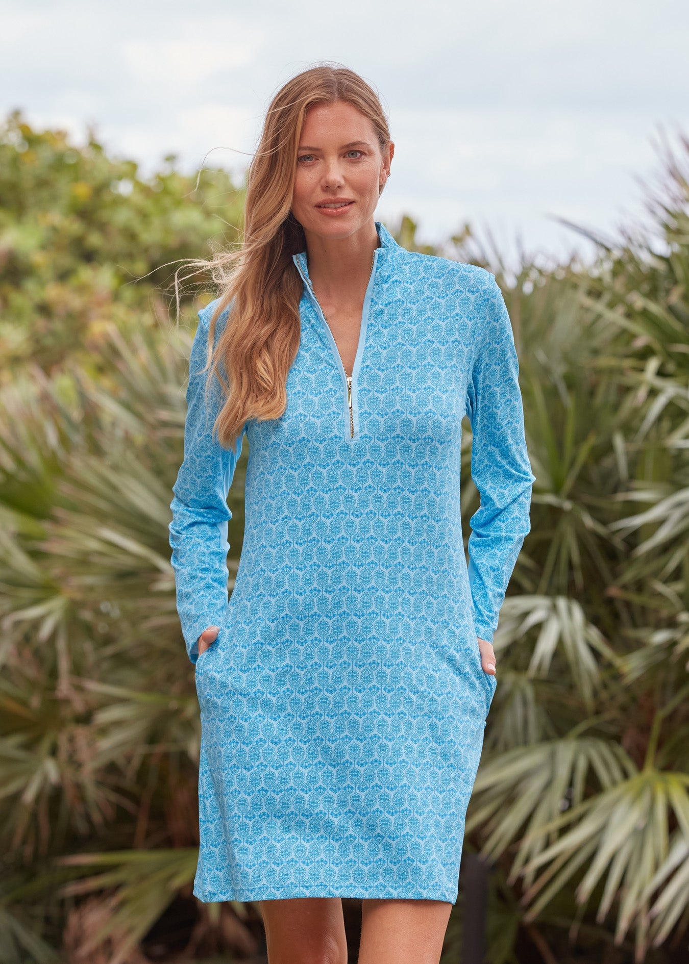 Woman wearing a blue patterned dress standing in front of green foliage