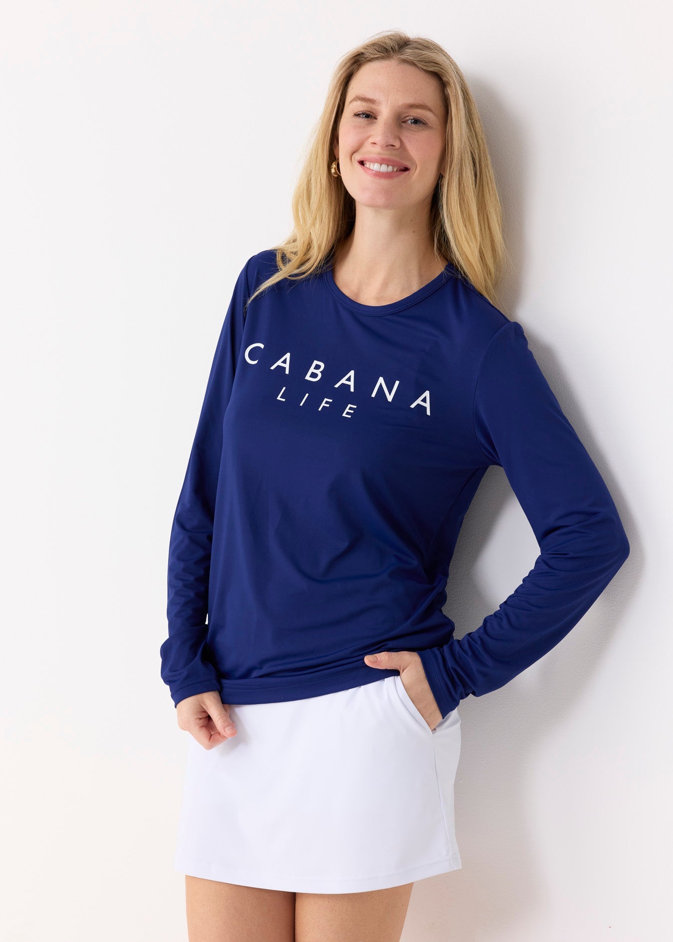 Woman wearing a blue 'Cabana Life' long-sleeve shirt and white skirt against a white background