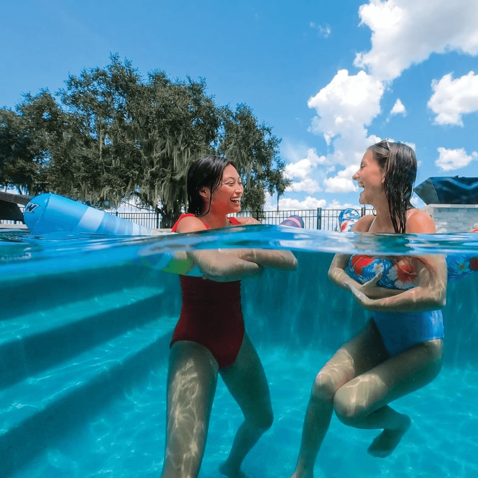 Two children playing in a pool with a blue sky and greenery in the background.