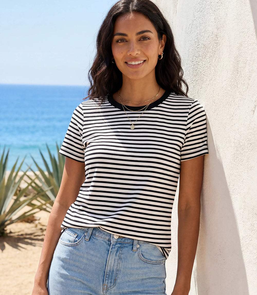 Woman wearing a black and white striped shirt and blue jeans standing by a beach.