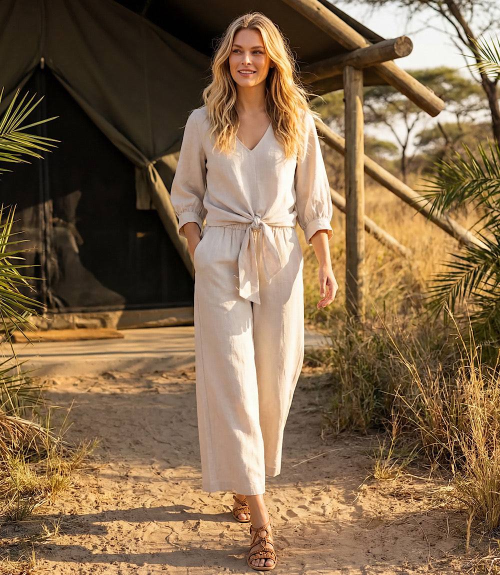 Woman in a beige outfit standing in front of a tent in a natural setting